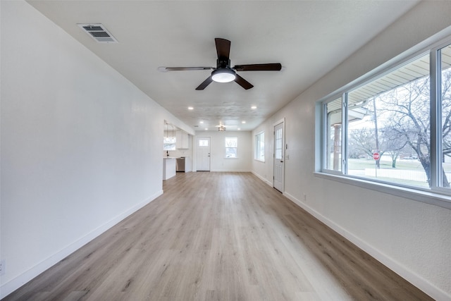 unfurnished living room with light wood-style floors, visible vents, ceiling fan, and baseboards