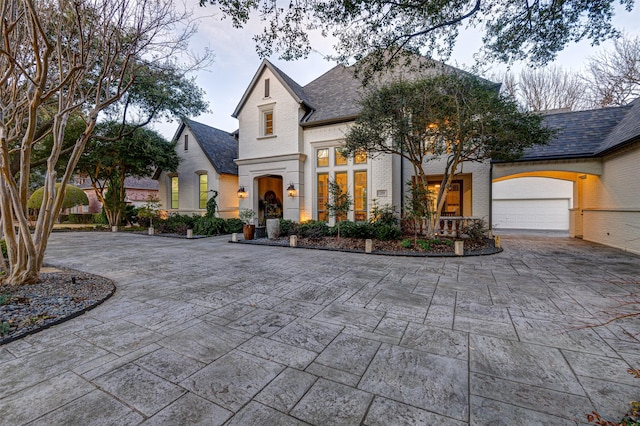 french country inspired facade featuring driveway, an attached garage, and brick siding