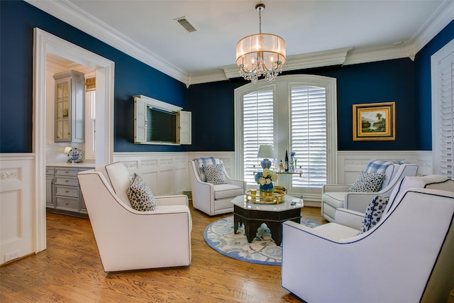 living area with a wainscoted wall, ornamental molding, visible vents, and an inviting chandelier