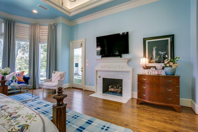 bedroom with crown molding, a fireplace, visible vents, wood finished floors, and baseboards