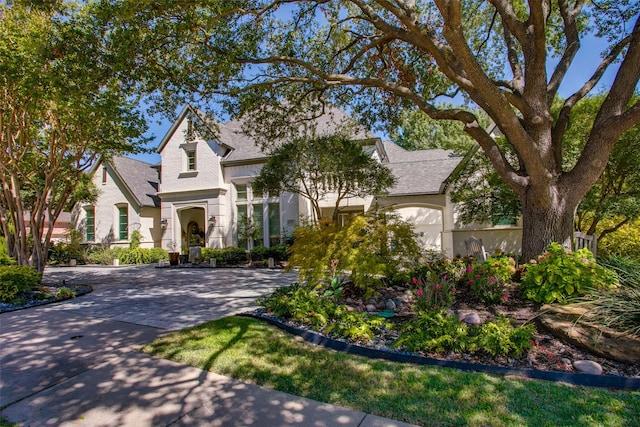 french country inspired facade with driveway, roof with shingles, and stucco siding