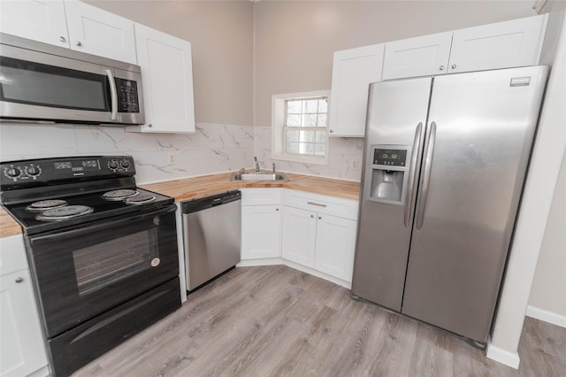 kitchen with stainless steel appliances, butcher block counters, white cabinetry, and a sink