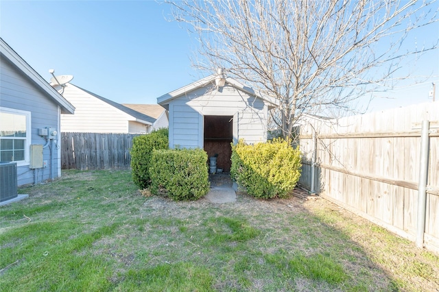 view of yard featuring a storage shed, a fenced backyard, central AC unit, and an outbuilding