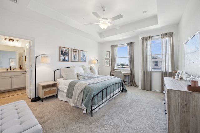 bedroom with a tray ceiling, ensuite bath, a ceiling fan, and light colored carpet