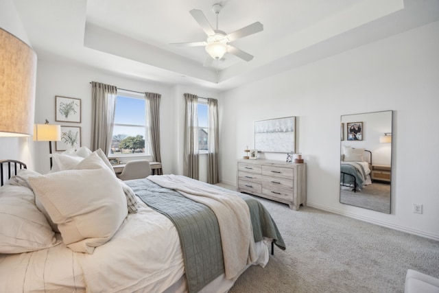 bedroom featuring light carpet, baseboards, a tray ceiling, and a ceiling fan