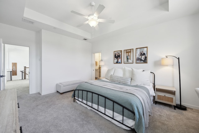 bedroom featuring light carpet, visible vents, a tray ceiling, and baseboards