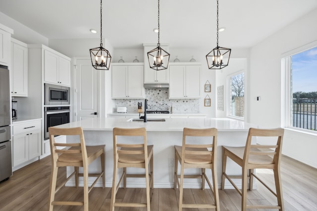 kitchen featuring stainless steel appliances, light countertops, a center island with sink, and white cabinets