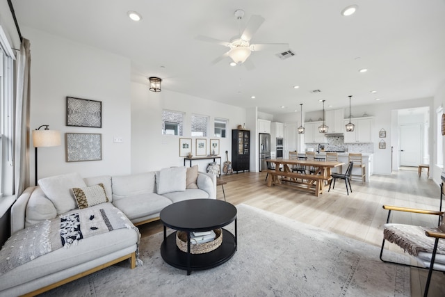 living area with light wood-style floors, ceiling fan, visible vents, and recessed lighting