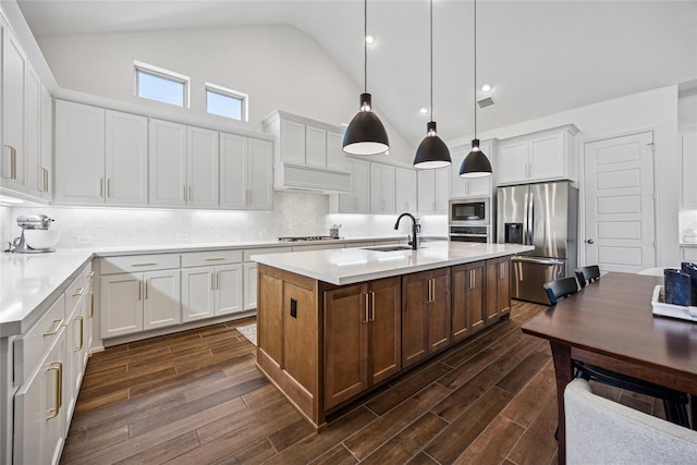 kitchen featuring stainless steel appliances, light countertops, a kitchen island with sink, and pendant lighting