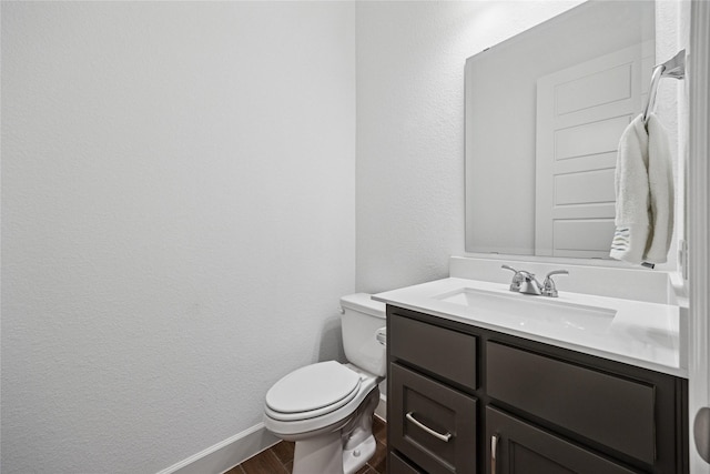 half bathroom featuring a textured wall, toilet, wood finished floors, vanity, and baseboards