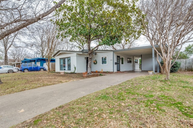 view of front of property with concrete driveway, an attached carport, a front yard, and fence