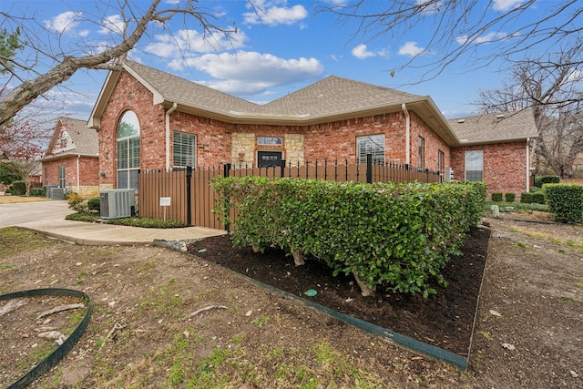 view of side of property featuring brick siding, a fenced front yard, and central AC unit