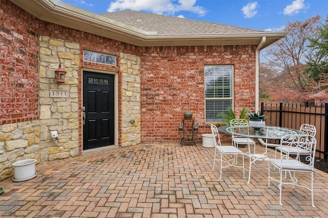 doorway to property featuring brick siding, a shingled roof, outdoor dining space, a patio area, and fence