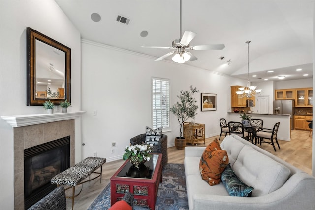 living area featuring visible vents, baseboards, a tile fireplace, light wood-style flooring, and vaulted ceiling