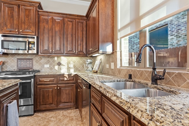 kitchen with a sink, ornamental molding, appliances with stainless steel finishes, decorative backsplash, and light stone countertops