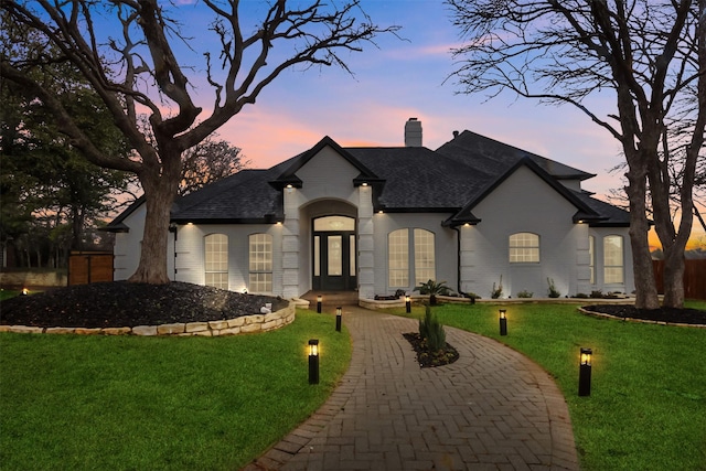 french provincial home with roof with shingles, brick siding, a chimney, and a front yard