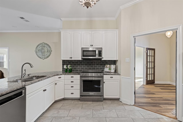 kitchen featuring crown molding, dark stone counters, white cabinets, stainless steel appliances, and a sink