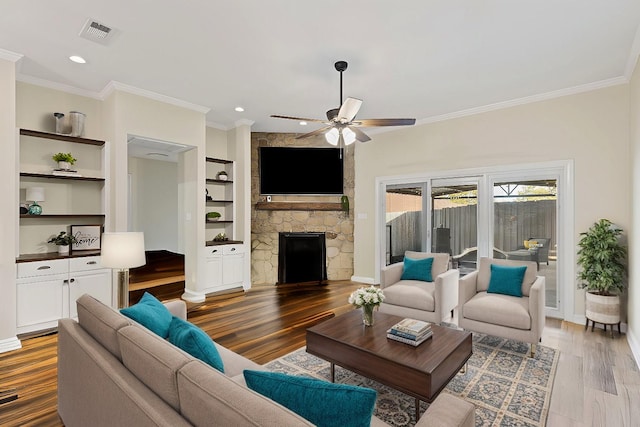 living area featuring built in shelves, a stone fireplace, wood finished floors, and ornamental molding