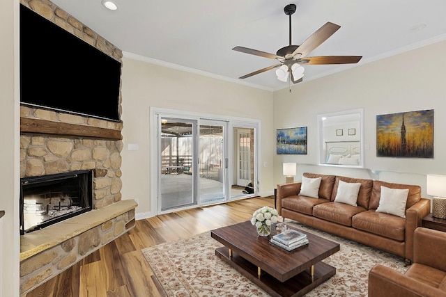 living area featuring a ceiling fan, wood finished floors, baseboards, a fireplace, and ornamental molding