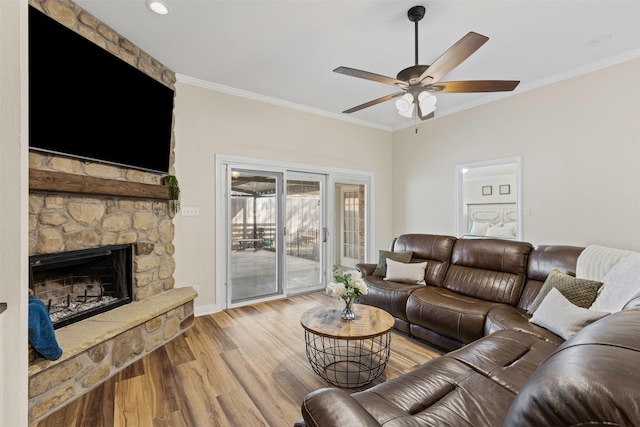 living area featuring a stone fireplace, crown molding, wood finished floors, and a ceiling fan