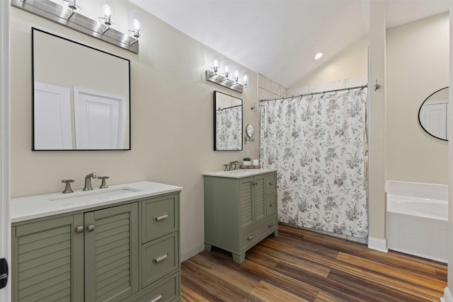 full bath with wood finished floors, two vanities, a sink, vaulted ceiling, and a washtub