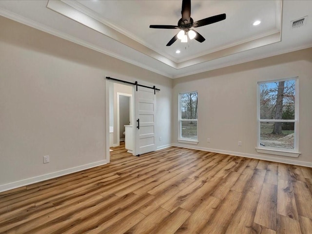 unfurnished bedroom featuring light wood finished floors, a barn door, visible vents, and a raised ceiling