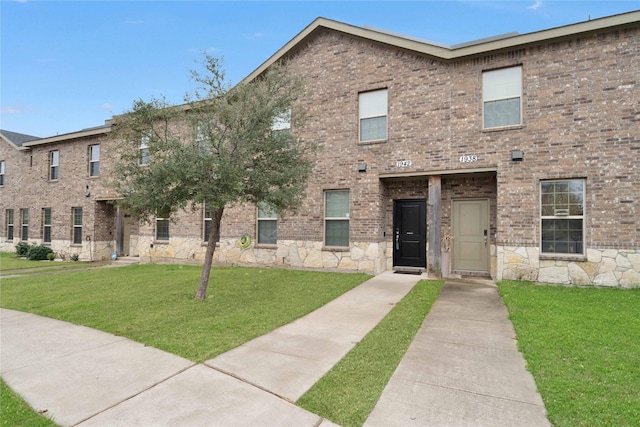 townhome / multi-family property with stone siding, brick siding, and a front yard