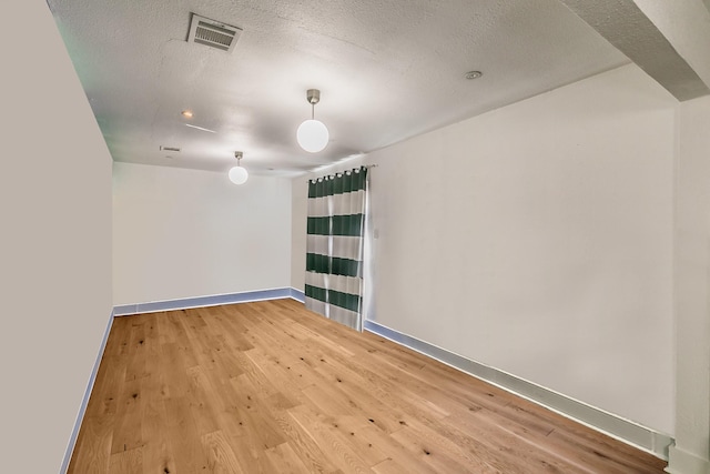 empty room with baseboards, light wood-type flooring, and a textured ceiling