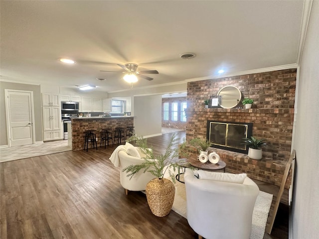 living area with crown molding, visible vents, a brick fireplace, ceiling fan, and wood finished floors