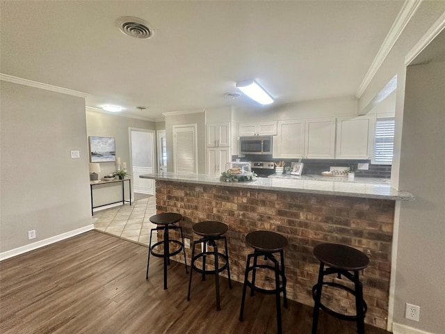 kitchen featuring visible vents, appliances with stainless steel finishes, white cabinetry, light wood-type flooring, and a peninsula