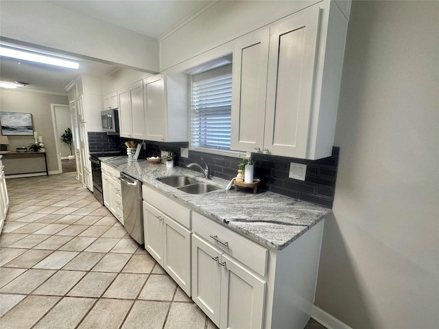 kitchen with appliances with stainless steel finishes, white cabinets, a sink, and backsplash