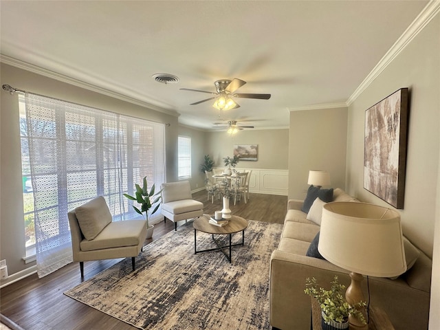 living area with visible vents, a ceiling fan, ornamental molding, wainscoting, and dark wood-style floors