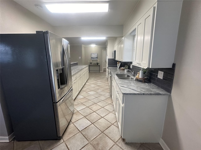 kitchen with a sink, white cabinets, light stone countertops, tasteful backsplash, and stainless steel fridge