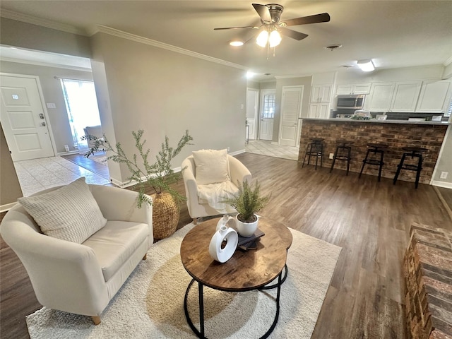 living area with baseboards, crown molding, light wood finished floors, and ceiling fan