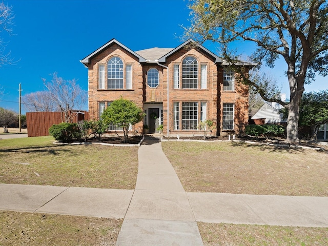 view of front of house with brick siding, a front lawn, and fence