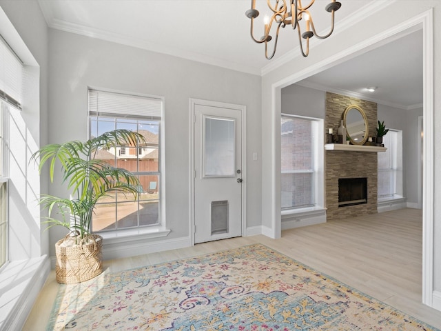 foyer with baseboards, ornamental molding, a fireplace, wood finished floors, and a notable chandelier