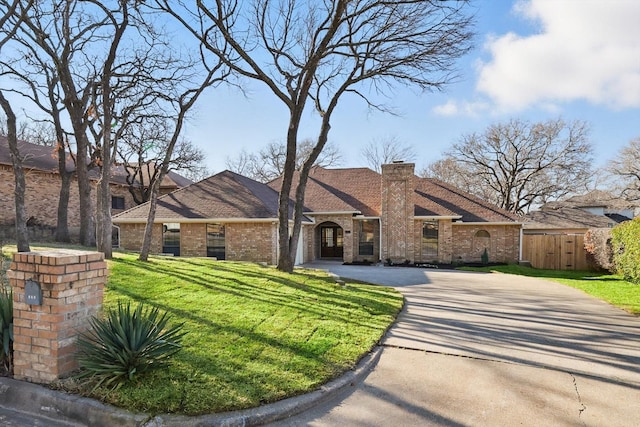 view of front of property with brick siding, fence, concrete driveway, a chimney, and a front yard