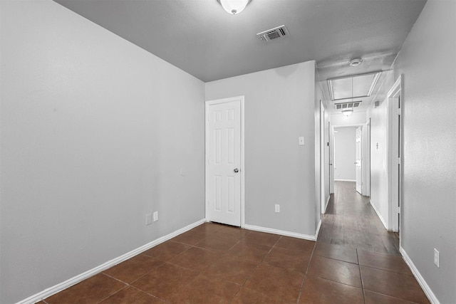 interior space featuring baseboards, dark tile patterned floors, visible vents, and attic access