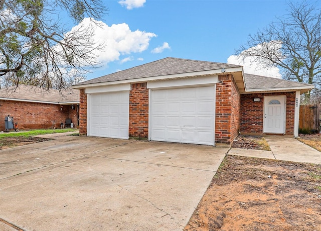 exterior space with a garage, driveway, brick siding, and roof with shingles