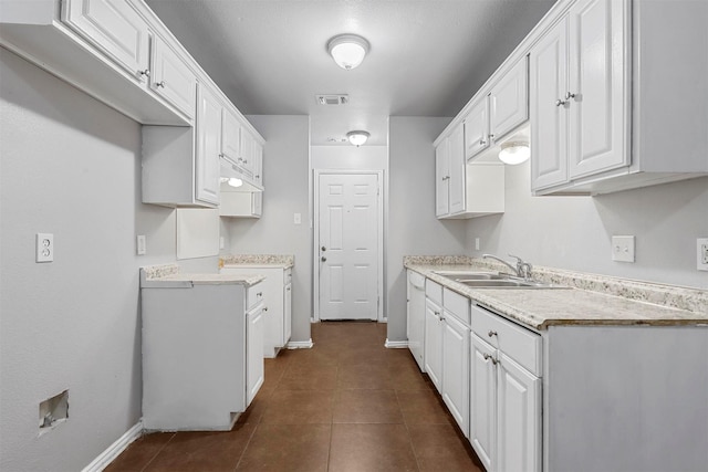 kitchen featuring light countertops, white cabinetry, a sink, dark tile patterned floors, and baseboards