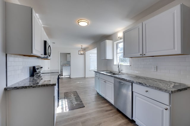 kitchen with dark stone countertops, a sink, light wood-type flooring, appliances with stainless steel finishes, and decorative backsplash