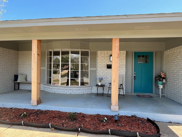 doorway to property with a porch and brick siding