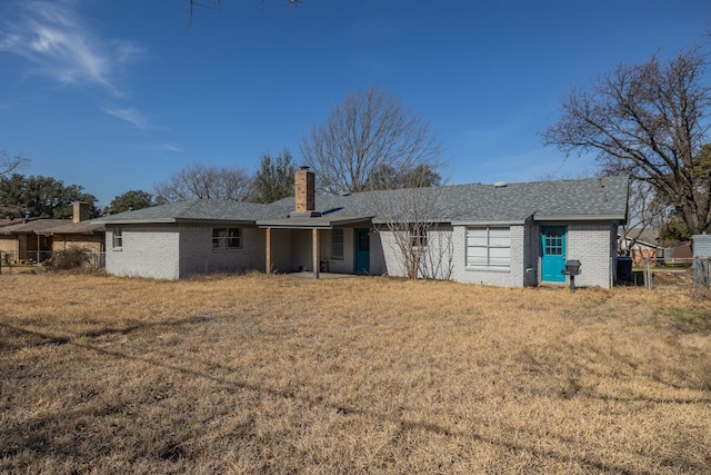 back of house with a yard, a chimney, brick siding, and fence
