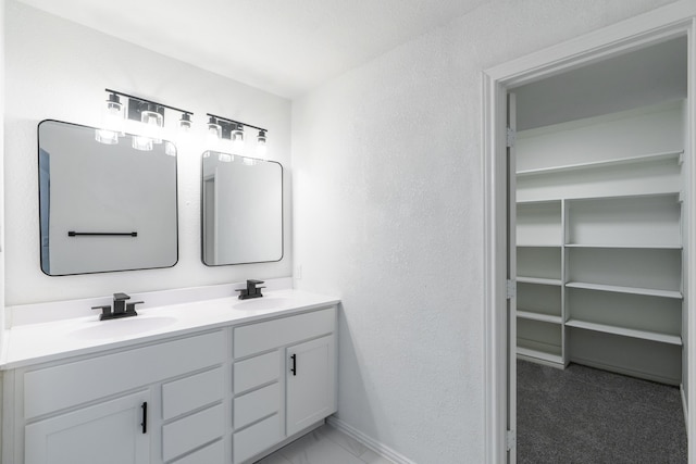 bathroom featuring a sink, double vanity, a walk in closet, and a textured wall