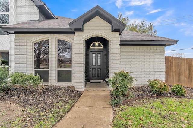 property entrance featuring roof with shingles, fence, and brick siding