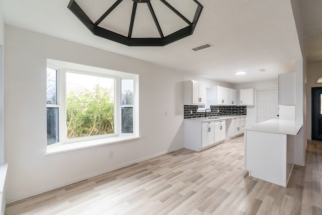 kitchen with visible vents, white cabinetry, baseboards, light countertops, and backsplash