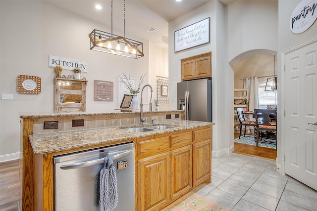 kitchen with arched walkways, stainless steel appliances, a sink, hanging light fixtures, and an island with sink