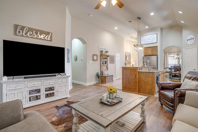 living room with high vaulted ceiling, ceiling fan, arched walkways, and light wood finished floors