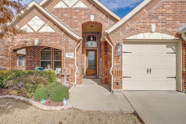 view of exterior entry with a garage, driveway, and brick siding