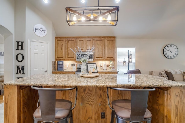 kitchen featuring arched walkways, light stone counters, stainless steel appliances, decorative backsplash, and brown cabinetry